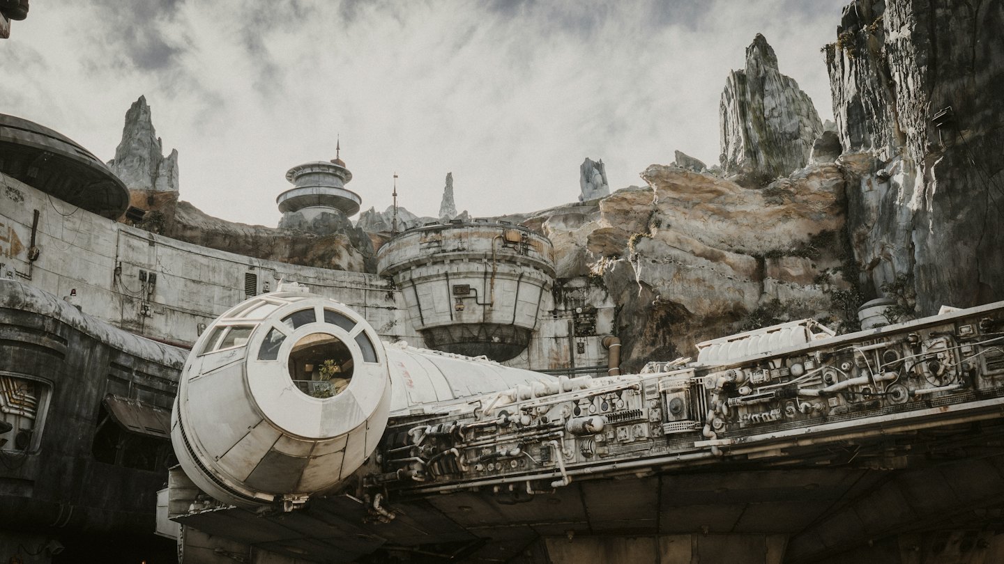Weathered spaceship parked in front of rocky mountains and buildings.