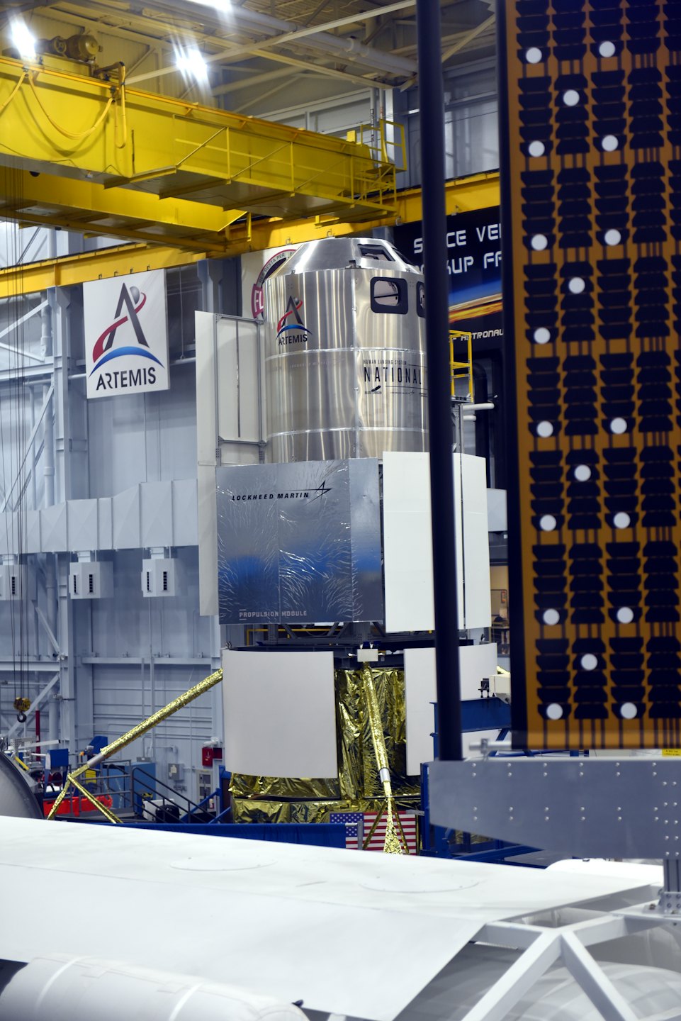Space capsule sits inside an industrial hangar for assembly.