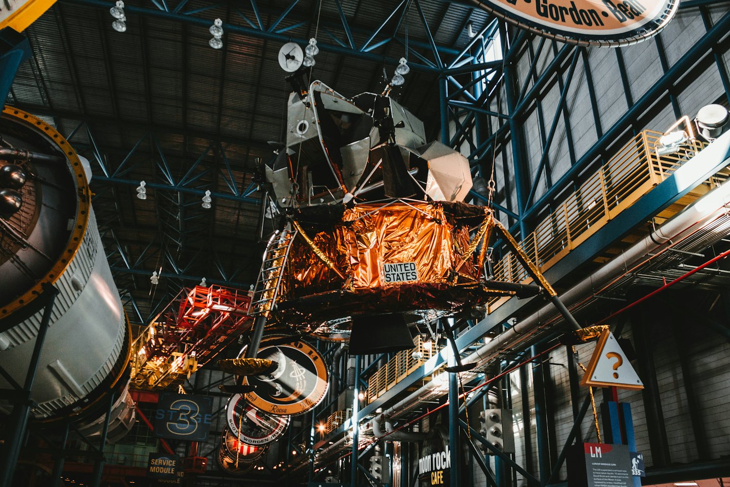 A golden lunar module hangs from the ceiling in an exhibition hall.