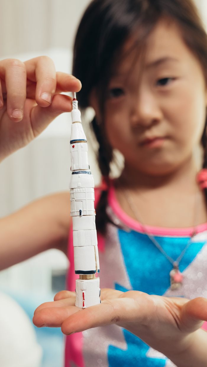 A young girl carefully holds a toy spacecraft, showing curiosity and imagination.